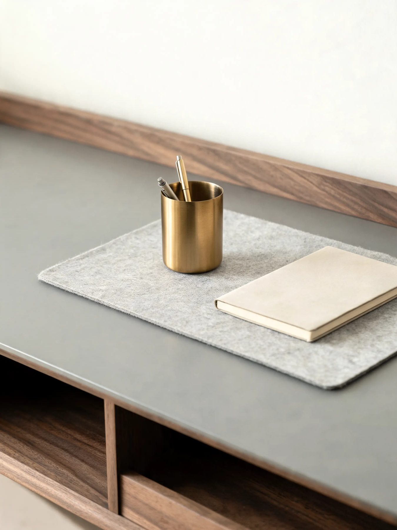 Walnut desk shelf with a felt mat and a brass pen cup on a matte grey desk